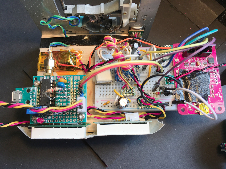 The complete electronics setup of the spectrograph. In the back
    there is the DVD drive stepper stage. In front of it, mounted on a piece of wood are a small USB-to-12V
    switching-regulator module to power the stepper motor in the top left, below on the bottom left is the
    photodiode preamp and on the right is a breadboard with the stepper driver module and lots of jumper wires
    interconnecting everything. On the right of the breadboard, a buspirate is attached to interface everything to a
    computer. On the bottom edge of the piece of wood, two LED panel meters are mounted for readout of the preamp
    output and the stepper supply voltages.